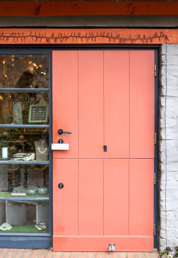 Fachada de comercio con puerta holandesa de madera en tono coral dotada de doble cerradura de seguridad.