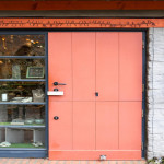 Fachada de comercio con puerta holandesa de madera en tono coral dotada de doble cerradura de seguridad.